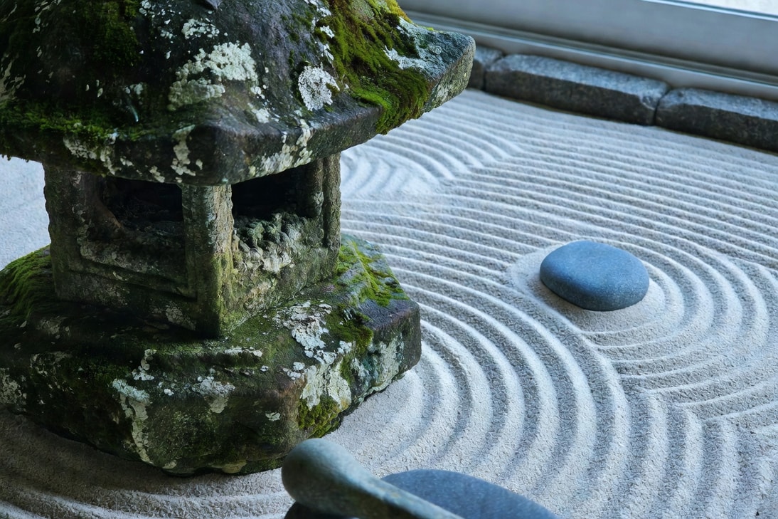 石燈籠特寫表面青苔地衣，斑駁質感如古銅，旁邊白砂波紋和青石。