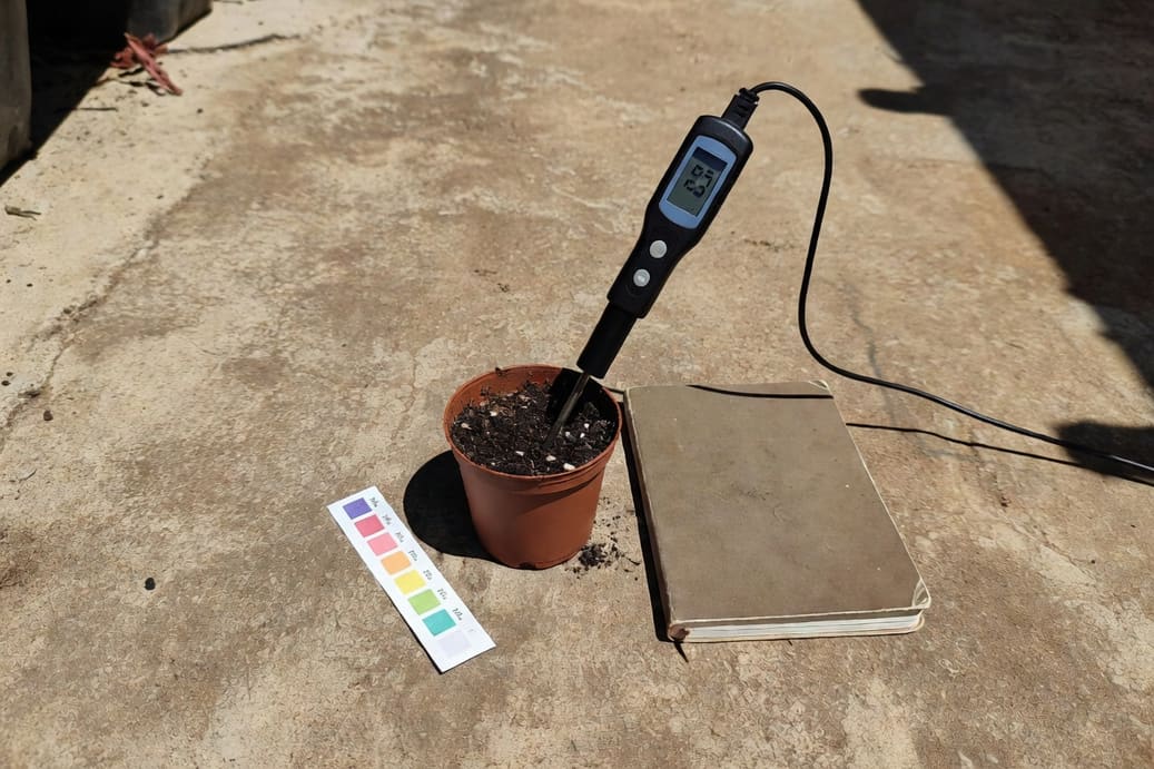 土壤EC測試儀插入盆栽介質，LCD顯示數值，旁邊有pH試紙和園藝筆記本。